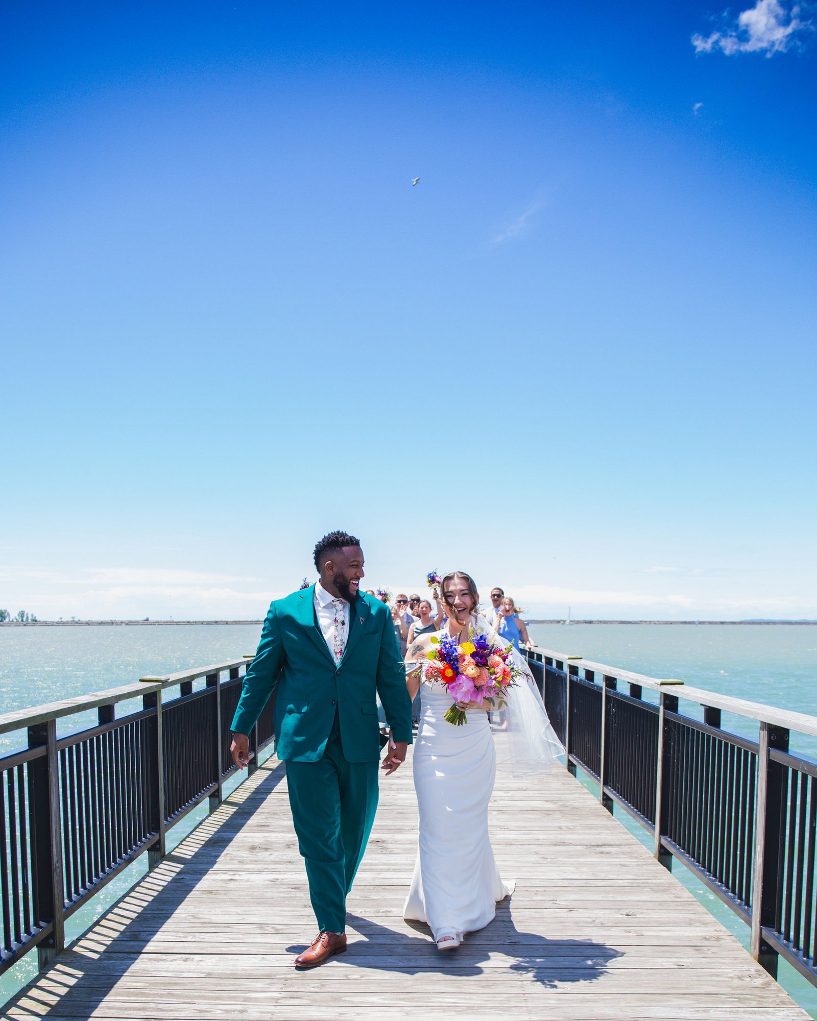 Bride and groom laughing as they walk down a pier by the water